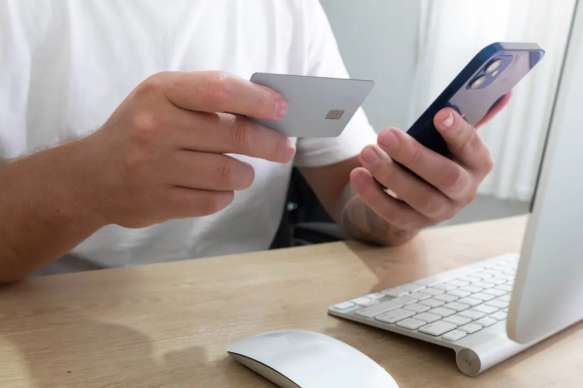 Manos sosteniendo un teléfono y una tarjeta bancaria en blanco