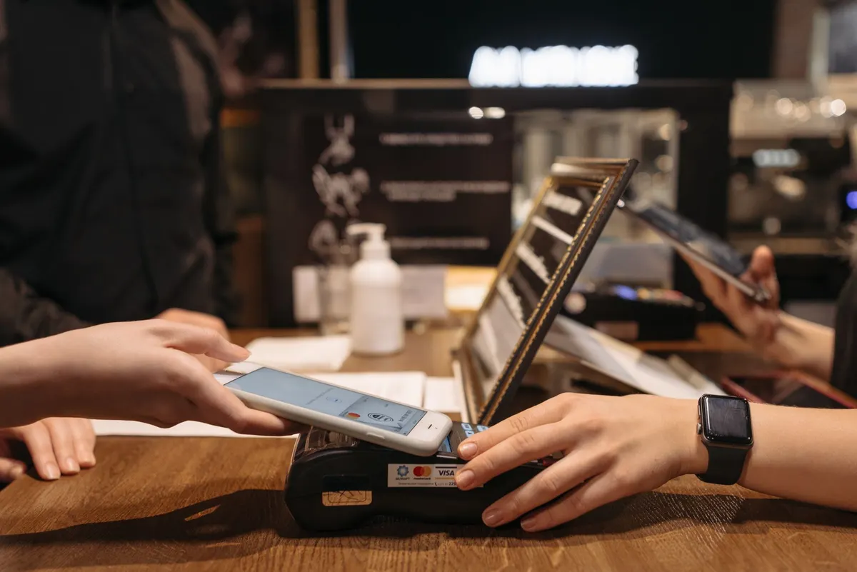 Mano acercando un teléfono a un terminal de pago con contactless