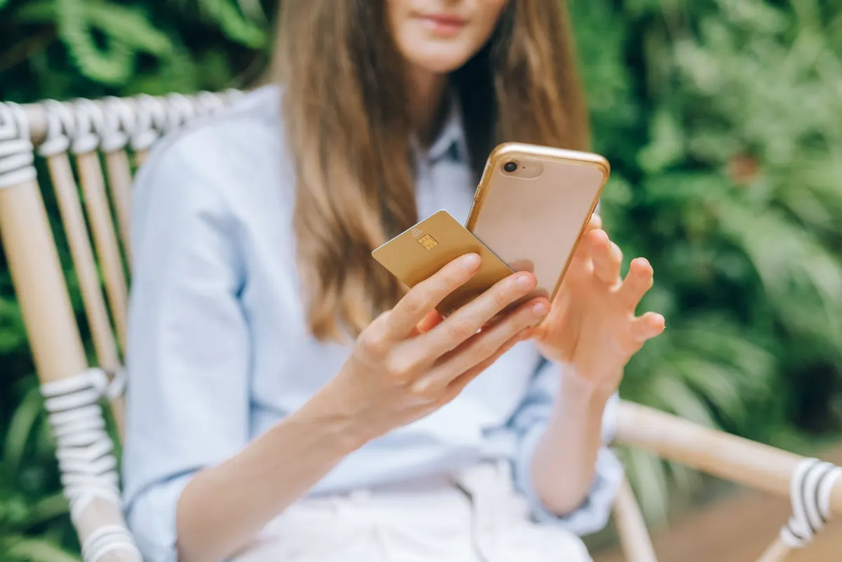 Mujer revisando su teléfono mientras sostiene una tarjeta dorada