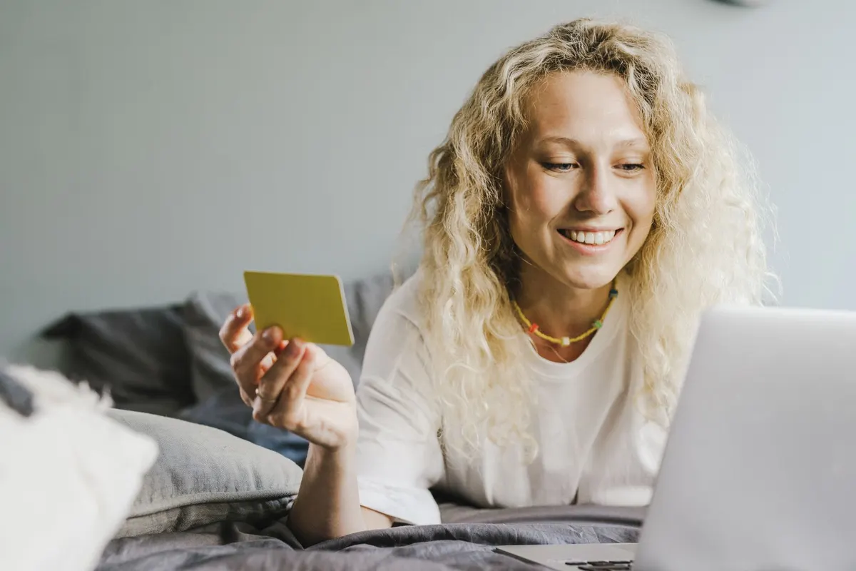 Mujer sonriente sosteniendo una tarjeta junto a su laptop