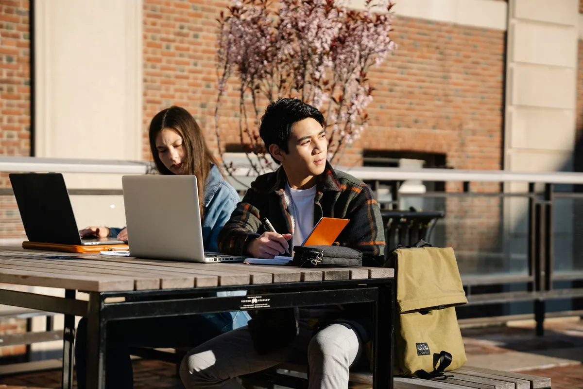 Dos estudiantes trabajando con sus laptops al aire libre