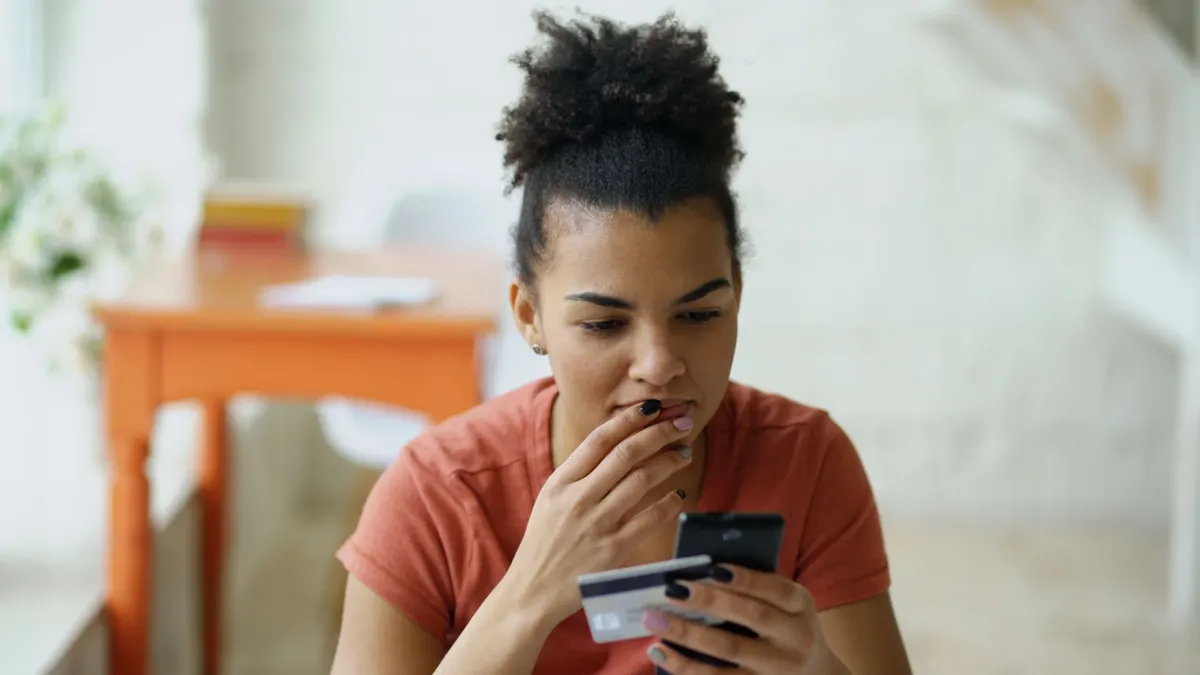 Mujer revisando su tarjeta y el teléfono con expresión de duda