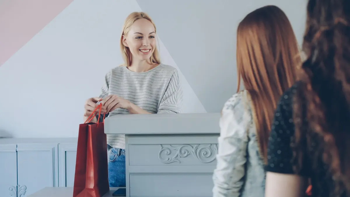 Vendedora entregando una bolsa de compra a dos clientas