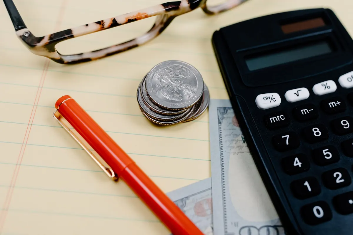 Calculadora, monedas y lentes sobre un cuaderno