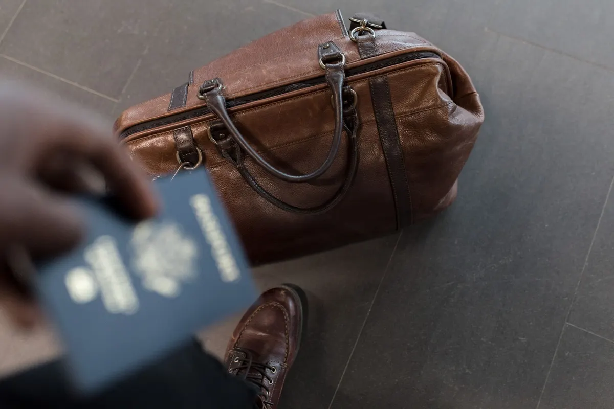 Persona sosteniendo un pasaporte junto a una maleta de viaje